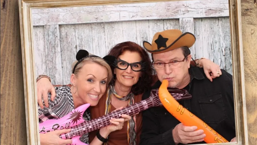 Gruppe von lachenden Gästen mit Gitarren und Cowboy‑Hut an der Snappix‑Fotobox